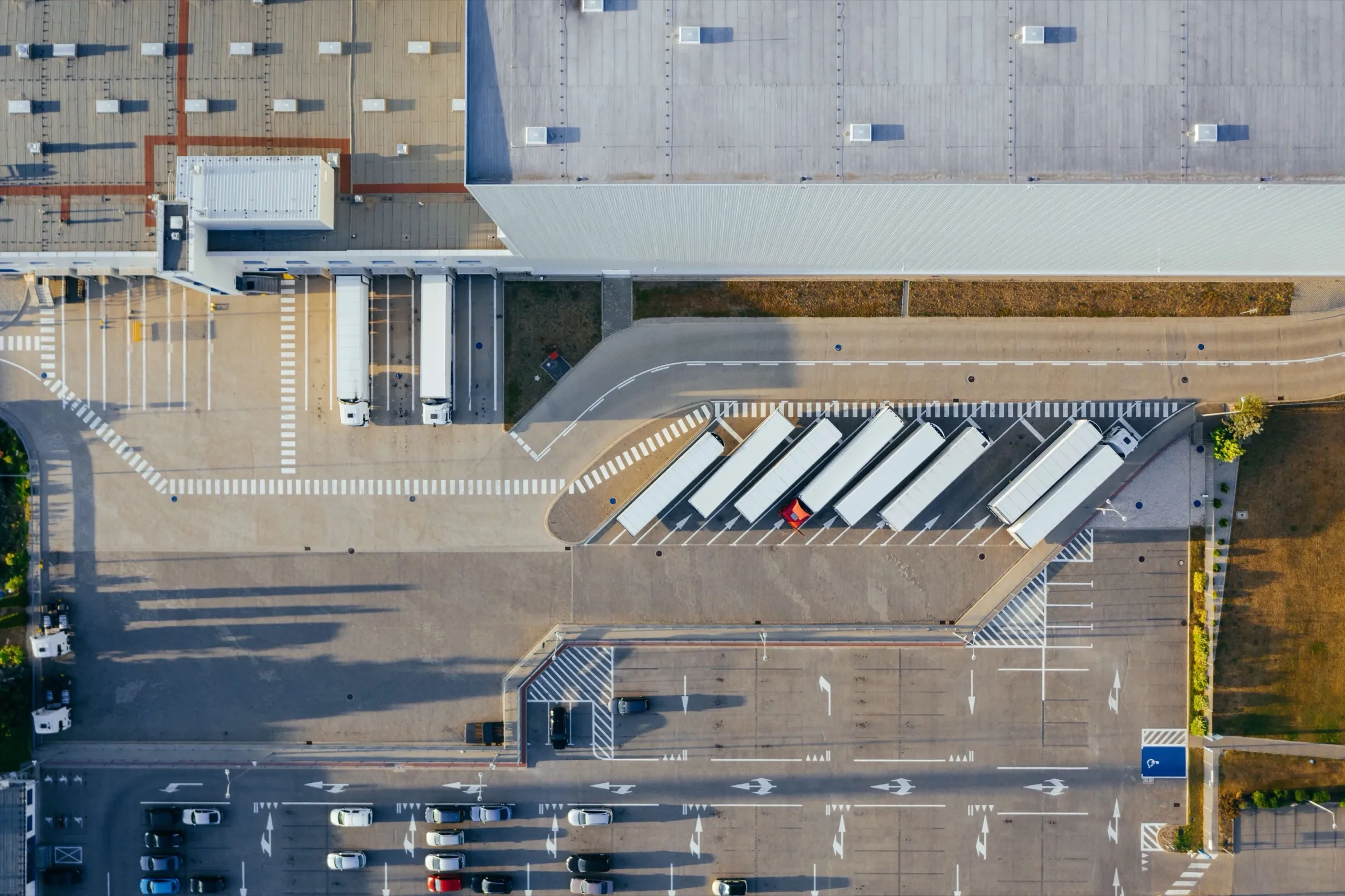 Luftbild eines Logistikzentrums: Hallendach, Lkw an den Rampen, abgestellte Auflieger auf dem Hof und ein Parkplatz.